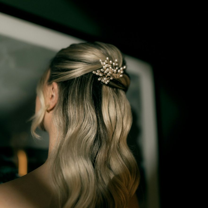 Half-up wavy blonde style with a pearl hair clip